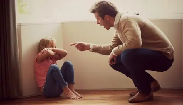 the boy is sitting on the floor and the man is yelling at him