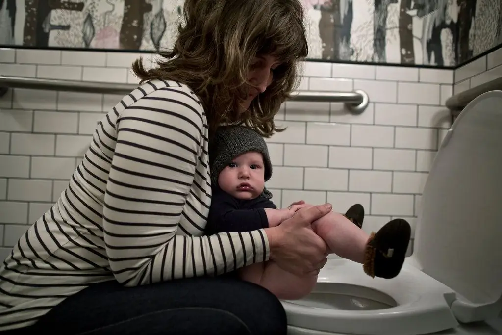 maman tenant bébé au-dessus des toilettes